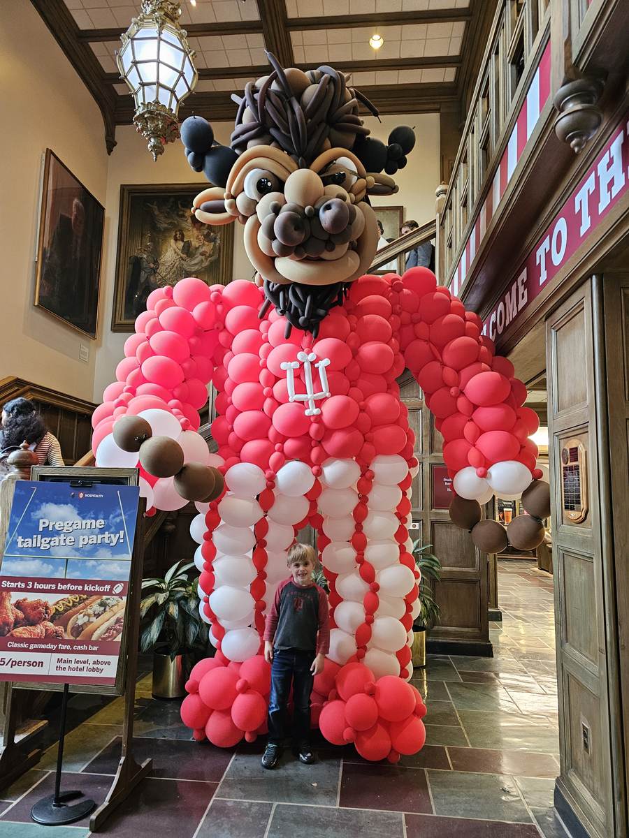 A child standing in front of a giant balloon sculpture of the IU mascot in the Hyatt Place Bloomington lobby, next to a sign advertising a pregame tailgate party