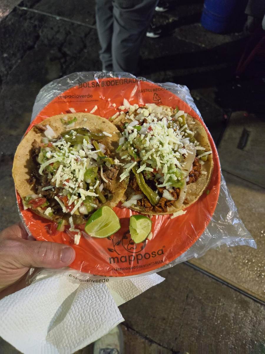 Two street tacos with onion, cilantro, cheese, and lime on an orange plate